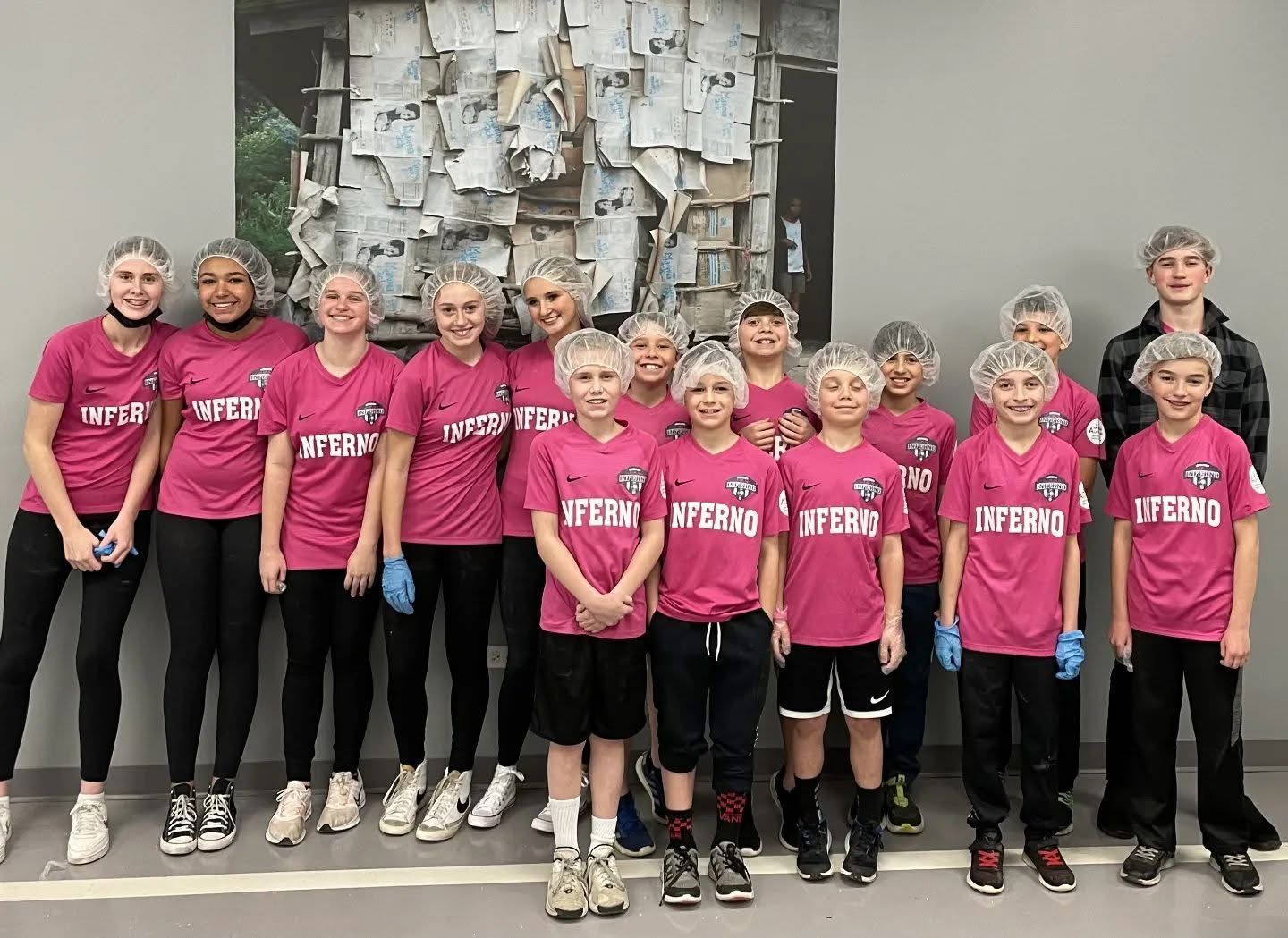 A group in pink jerseys and hairnets, standing in front of a wall with art.