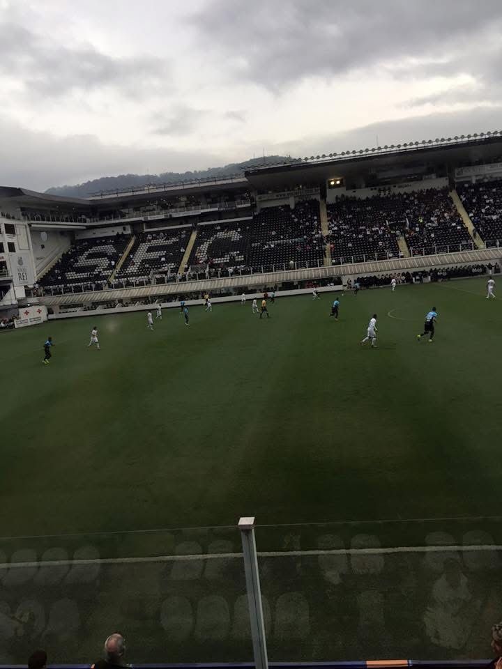 Soccer game in progress at a stadium with players on the green field.
