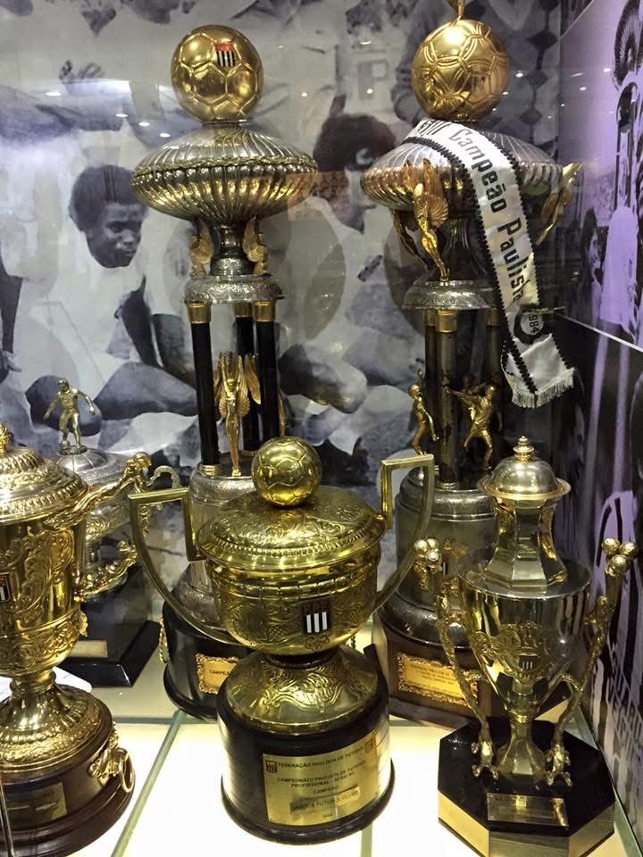 Trophies displayed in a glass case, including several gold and black trophy cups. Black and white background.