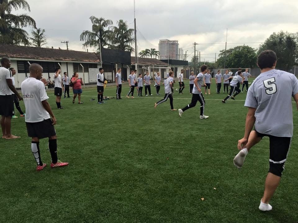 Soccer players in gray shirts and black shorts stretching on a green field.