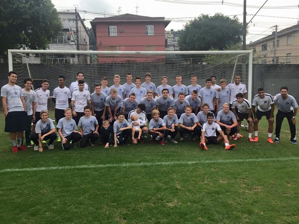 Soccer team posing on a green field in front of a goal. Players wear gray and white uniforms.