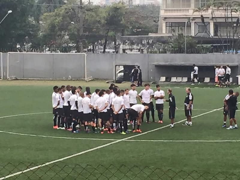 Soccer players in white and black uniforms on a green field, listening to coaches.