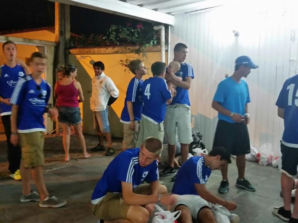 Group of people in blue soccer jerseys standing and sitting outdoors at night.