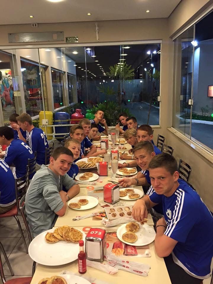 Group of boys in blue shirts eating at a restaurant, lit by interior and exterior lights.