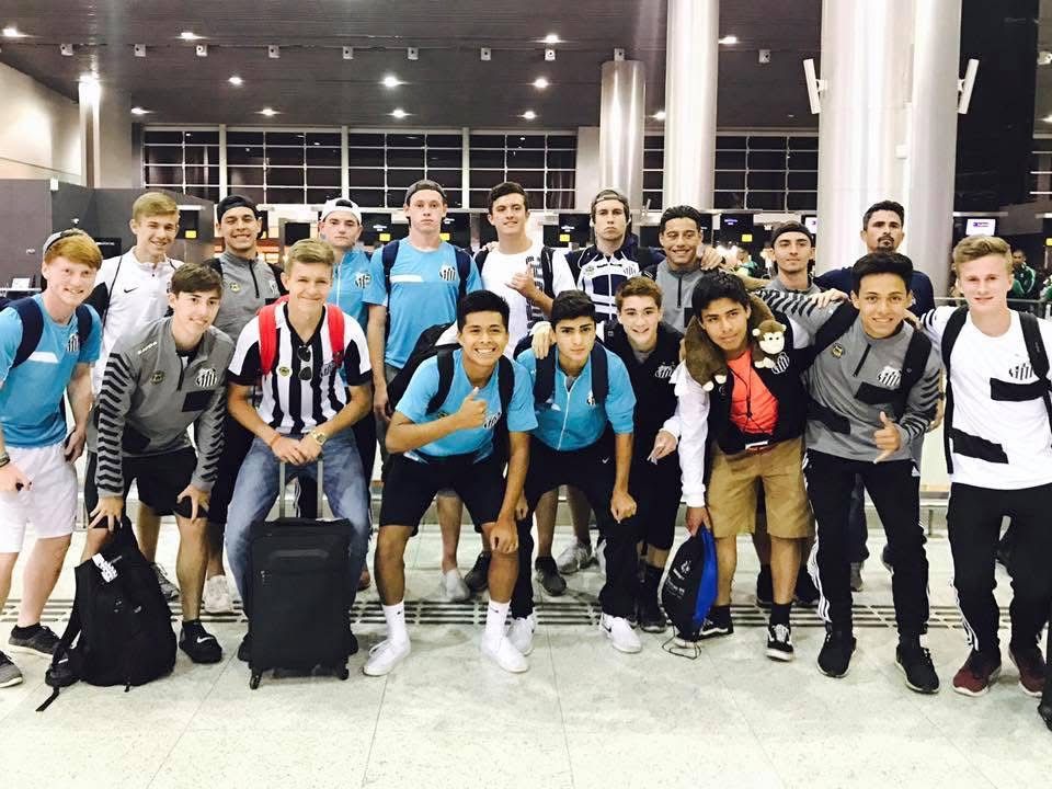 Group of young men in various outfits at an airport. Some are smiling, and many have backpacks.