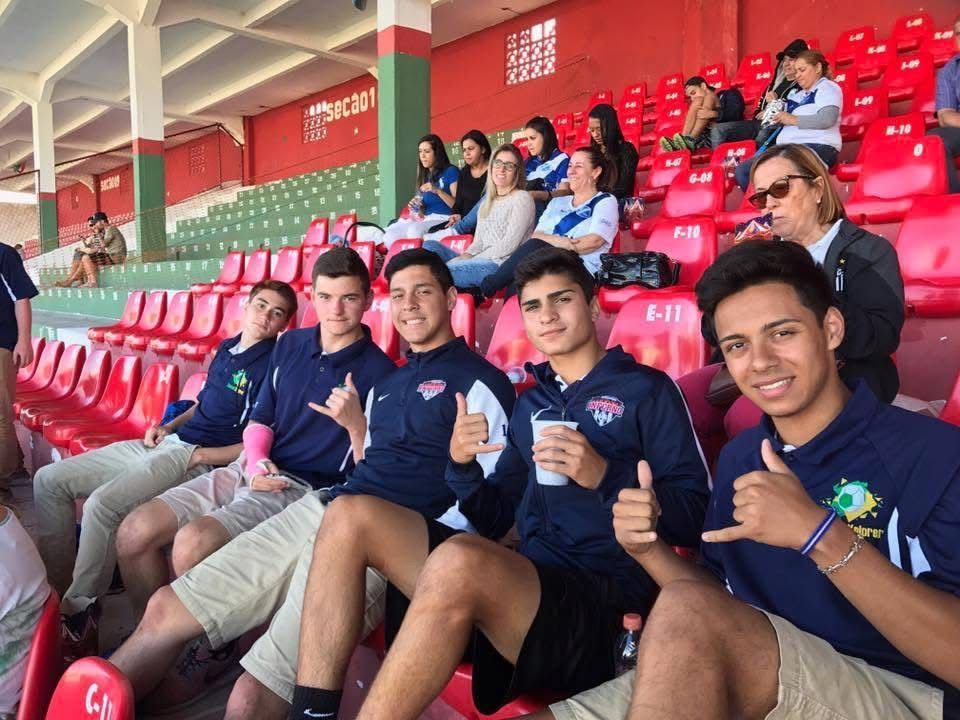 Group of young men in team jackets giving thumbs up, sitting in stadium seating.