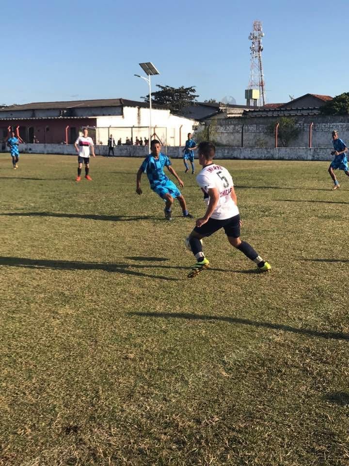 Soccer players on a field. One in white shirt dribbles the ball as another in a blue shirt approaches.