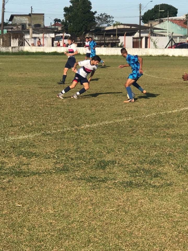 Soccer players on a green field; one in black and white attempts to dribble past a player in blue.