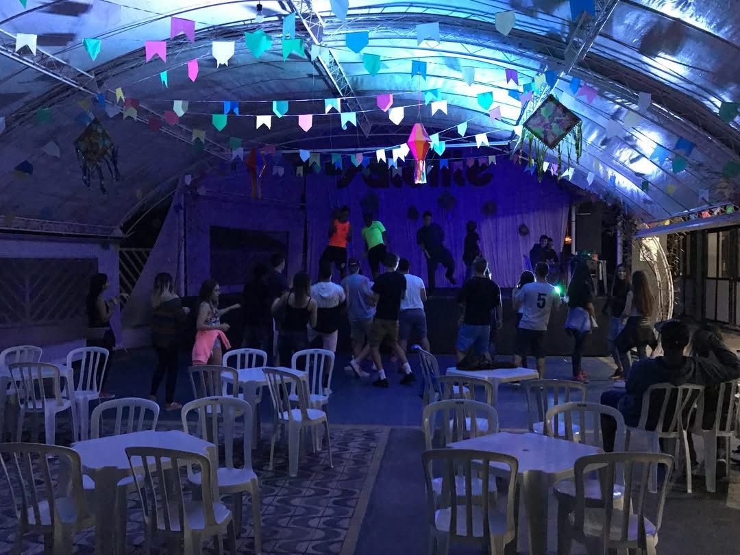 Party scene: people dancing at a venue decorated with colorful flags. Tables and chairs are in the foreground.