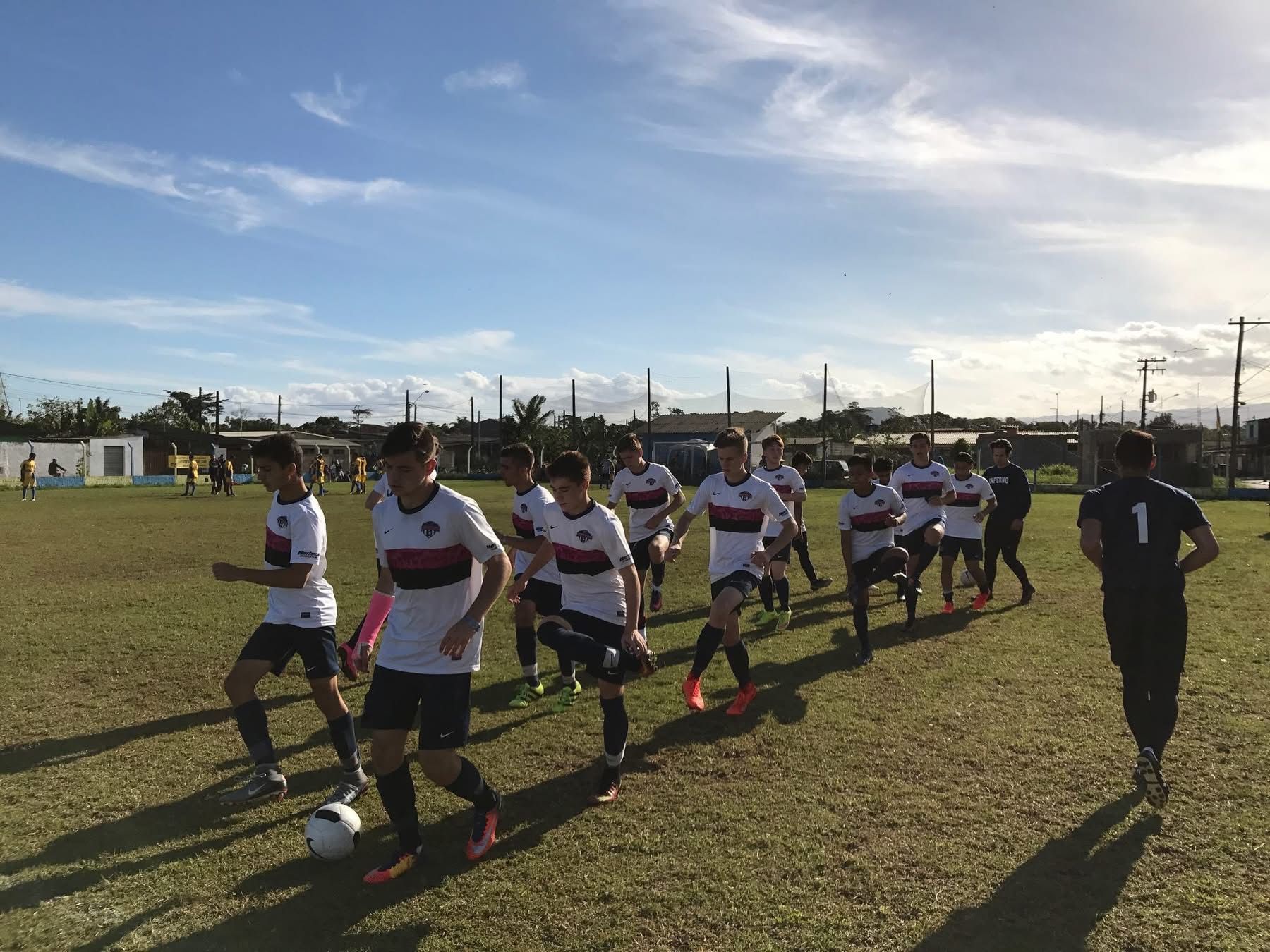 Soccer team in white and black uniforms running on a grass field under a blue sky.