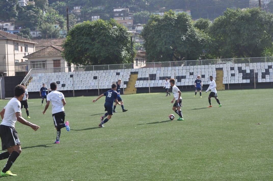 Soccer game on a green field. Players in white and blue uniforms compete, kicking a ball. Fenced stadium background.