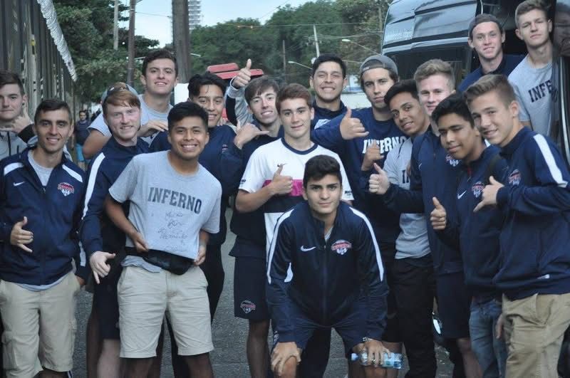 Group of young men in blue and white athletic wear, standing outdoors near a vehicle, smiling and giving thumbs up.