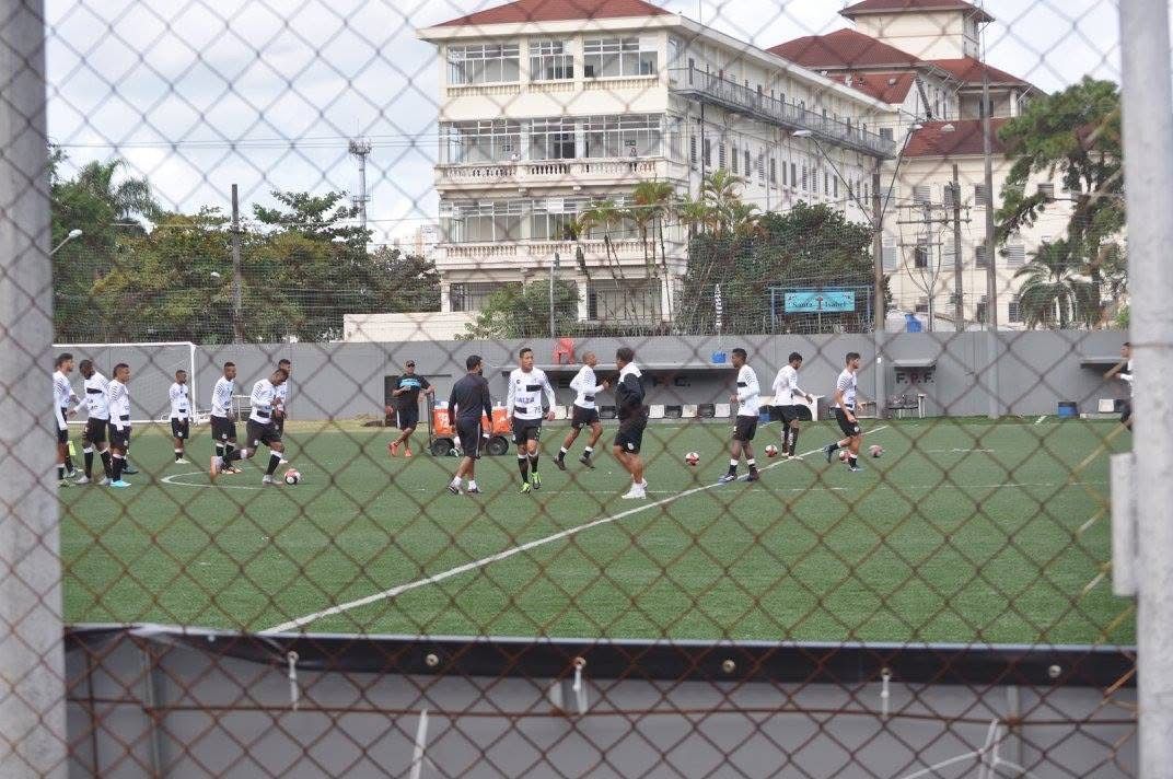 Soccer players on a green field, practicing. A large building in the background. Players wearing black and white.