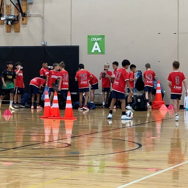 Soccer players in red jerseys on an indoor court, near orange cones, preparing for a game.