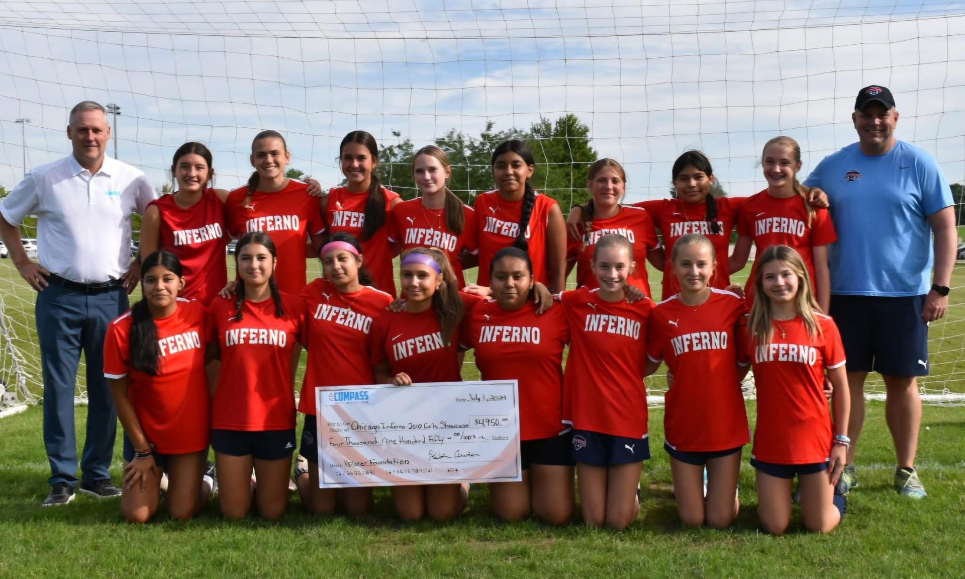 Soccer team in red shirts with coach and official, holding a check on a green field.