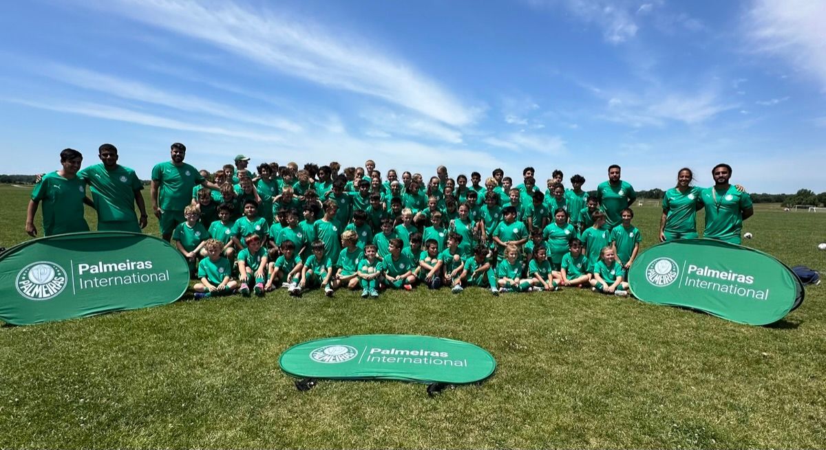 Group of people in green shirts pose on grass field under a blue sky, with event banners.