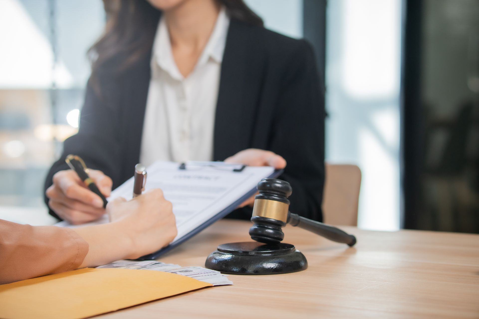 Person signing document; gavel on desk; another person holds clipboard. Person signing document; gavel on desk; another person holds clipboard.