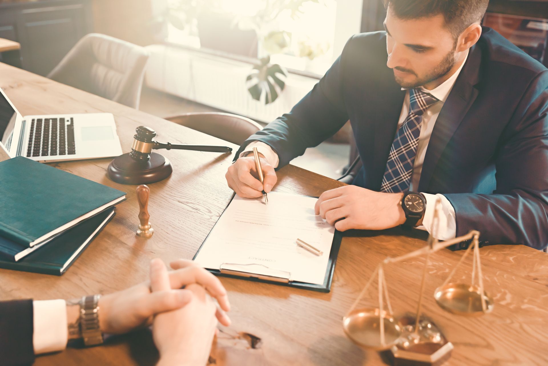 Man in suit signing documents at a desk, scales of justice and law books present.