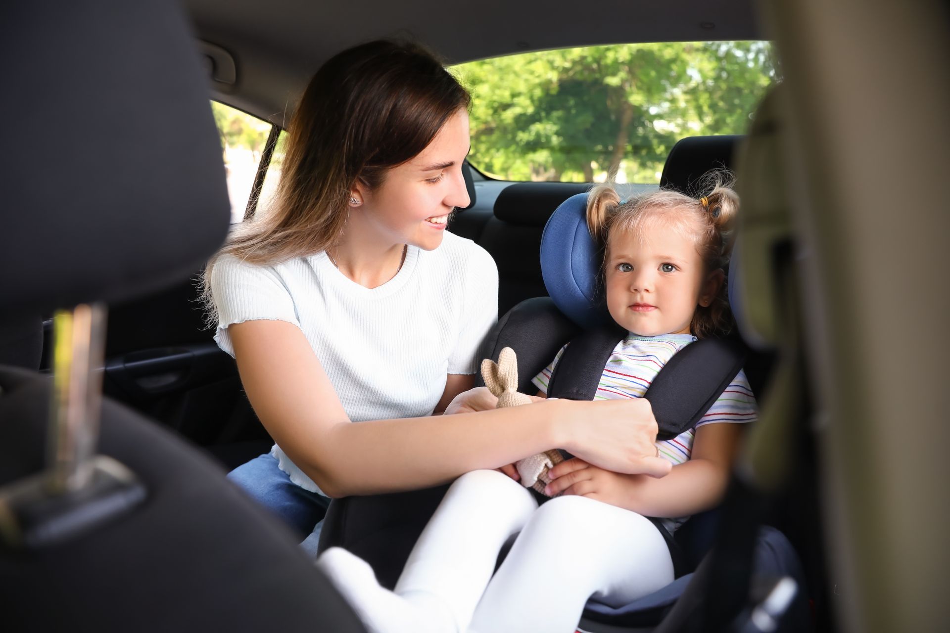 Woman buckling a child into a car seat in the backseat of a car. Woman buckling a child into a car seat in the backseat of a car.