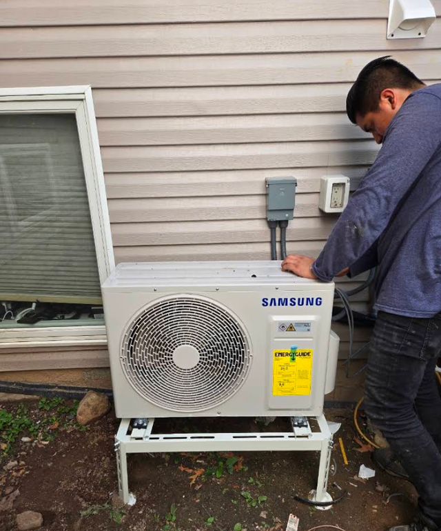 Technician working on a Samsung outdoor air conditioner unit beside a house exterior.