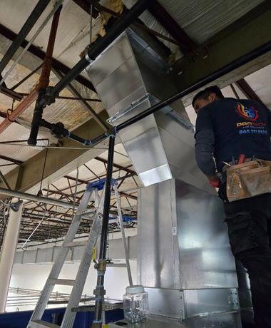 Worker installing shiny metal ductwork in a ceiling space at a construction site