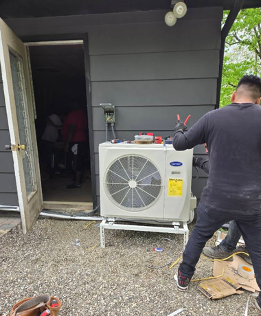 Technician working on an outdoor HVAC unit beside a house entrance