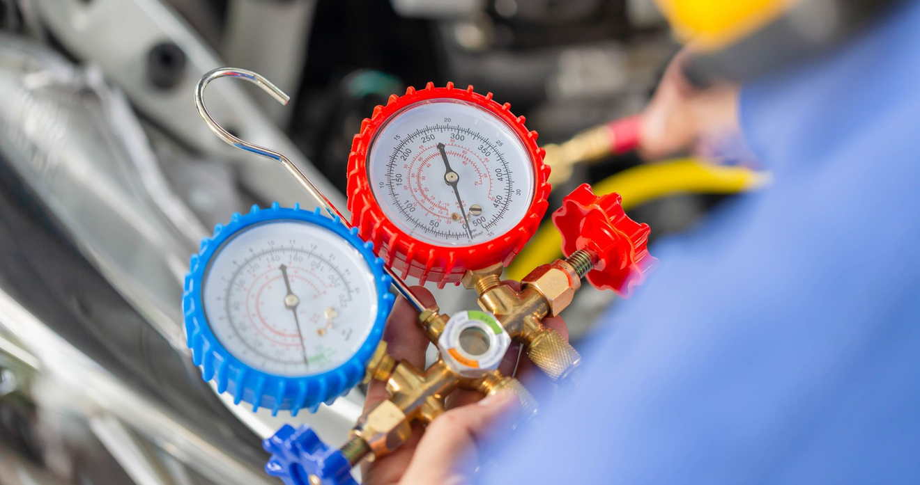 Blue and red gauges on HVAC manifold held near equipment during maintenance