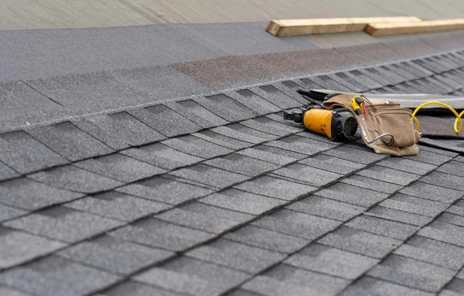 A roof with shingles being installed and tools on it.