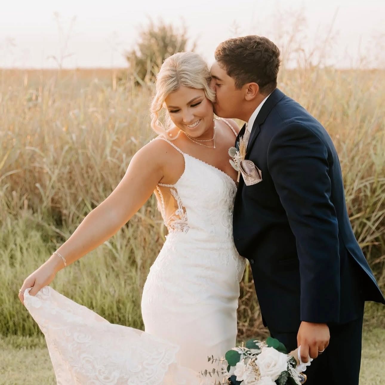 groom kissing bride in grassy field