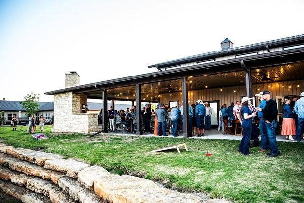 People mingling outside a rustic stone-and-wood event hall on a grassy lawn