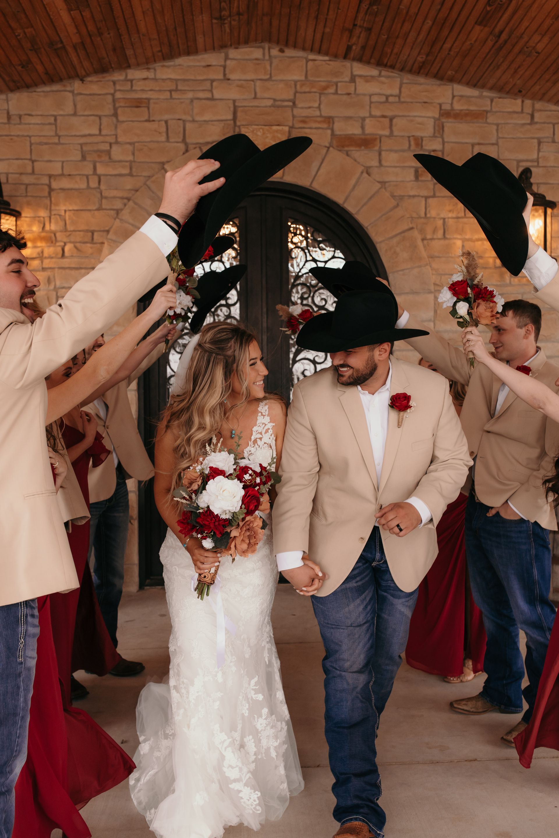bride and groom walking between wedding party's arms while they hold up cowboy hats