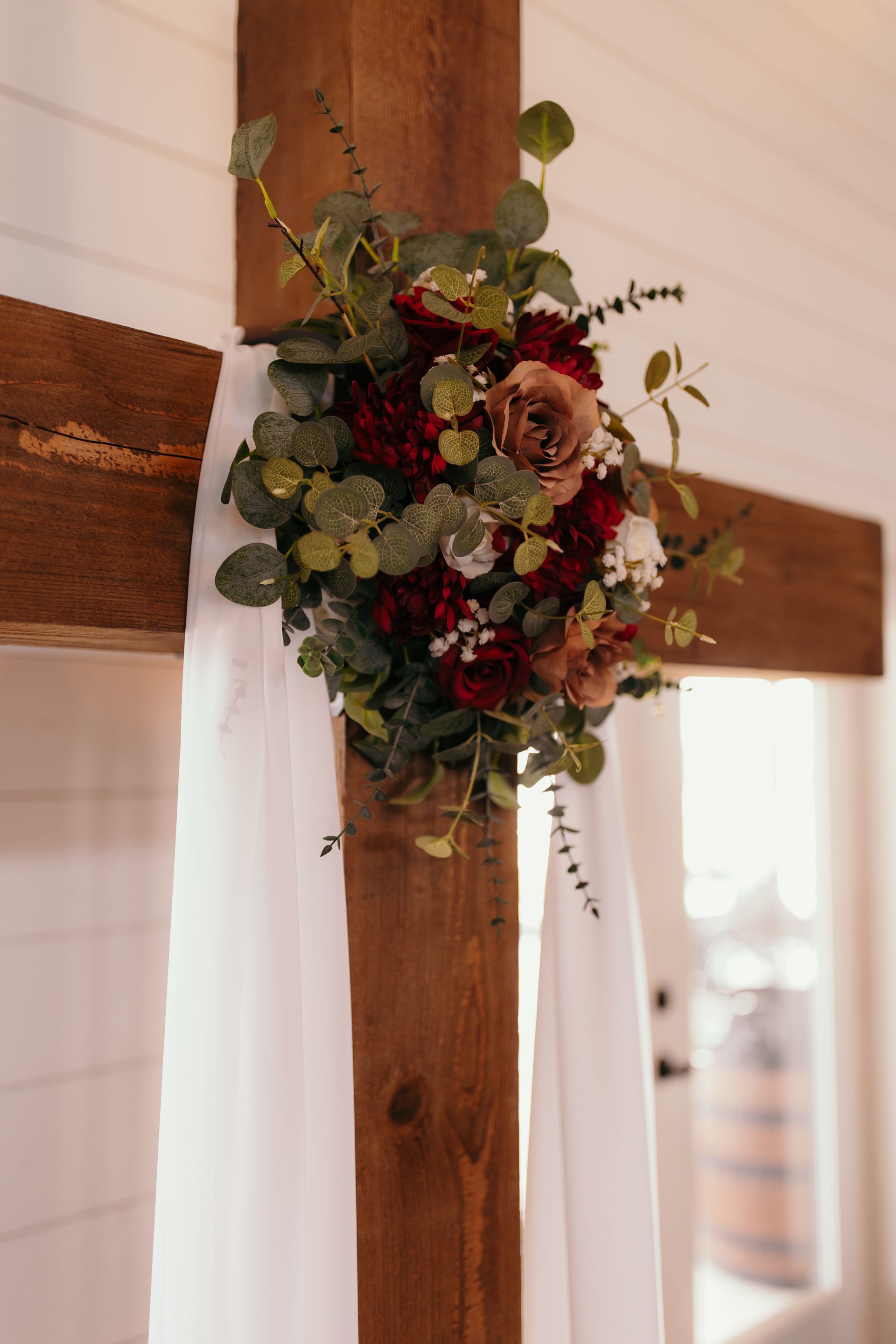 fall colored flower arrangement on wooden cross