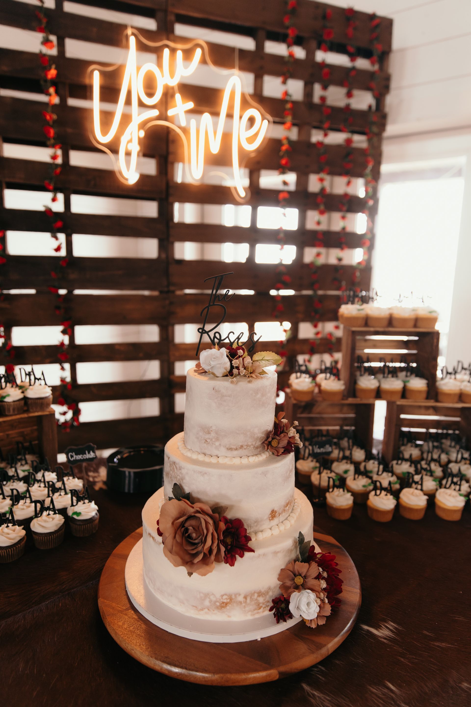 rustic three tier wedding cake and cupcakes with neon sign in the background