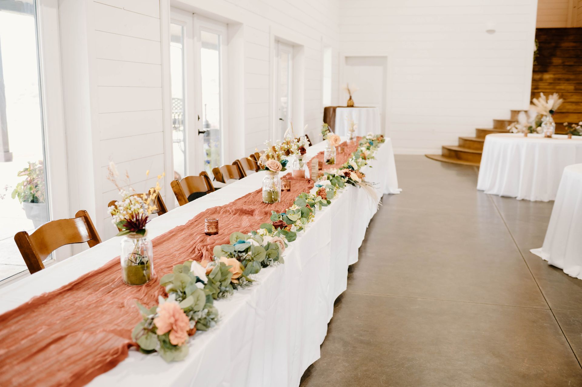 long wedding reception table with pink runner and wooden chairs