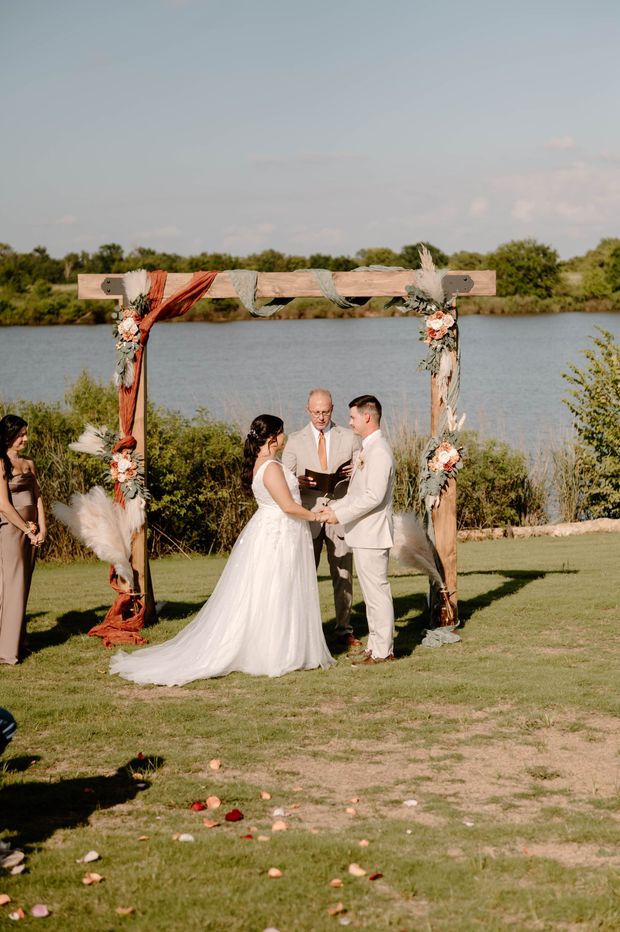 Outdoor wedding ceremony by a lake, with bride and groom standing under a floral arch.