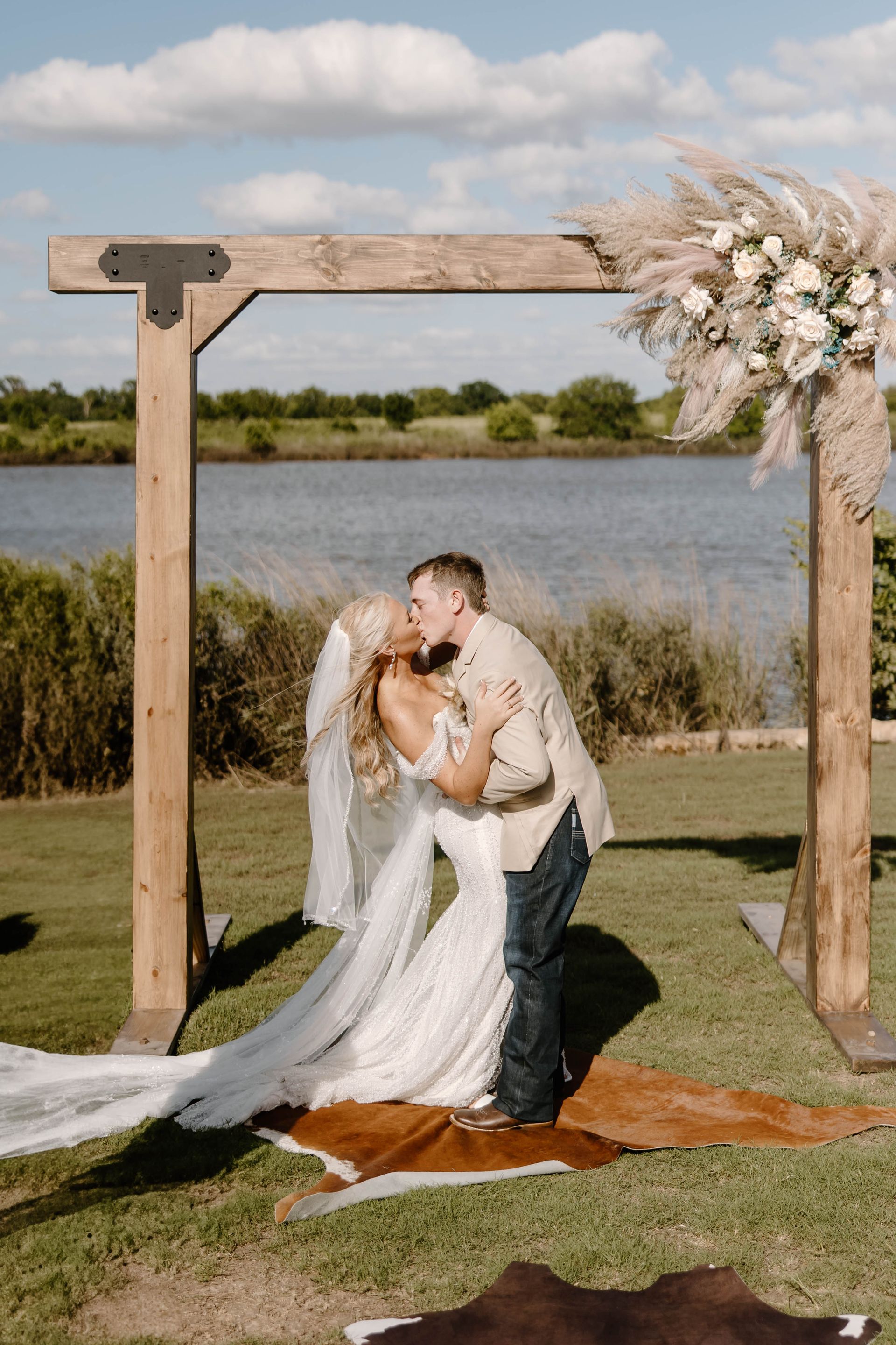 bride and groom kissing under wooden waterfront wedding arch