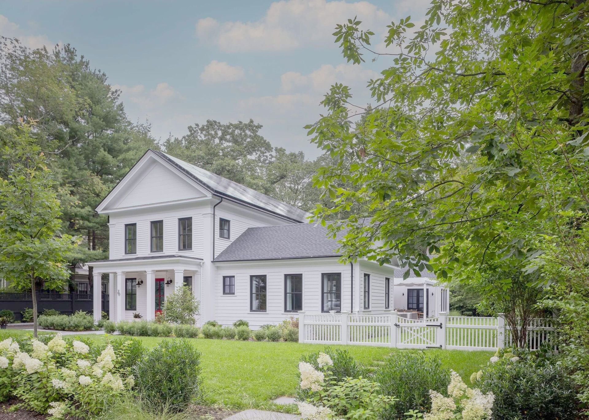 Front view of a New England Farmhouse with a manicured yard and trees framing the edges of the image.