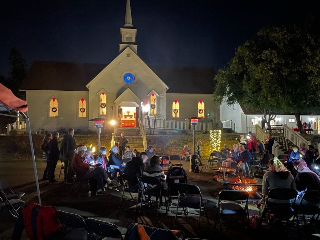 A group of people are sitting around a fire in front of a church at night.