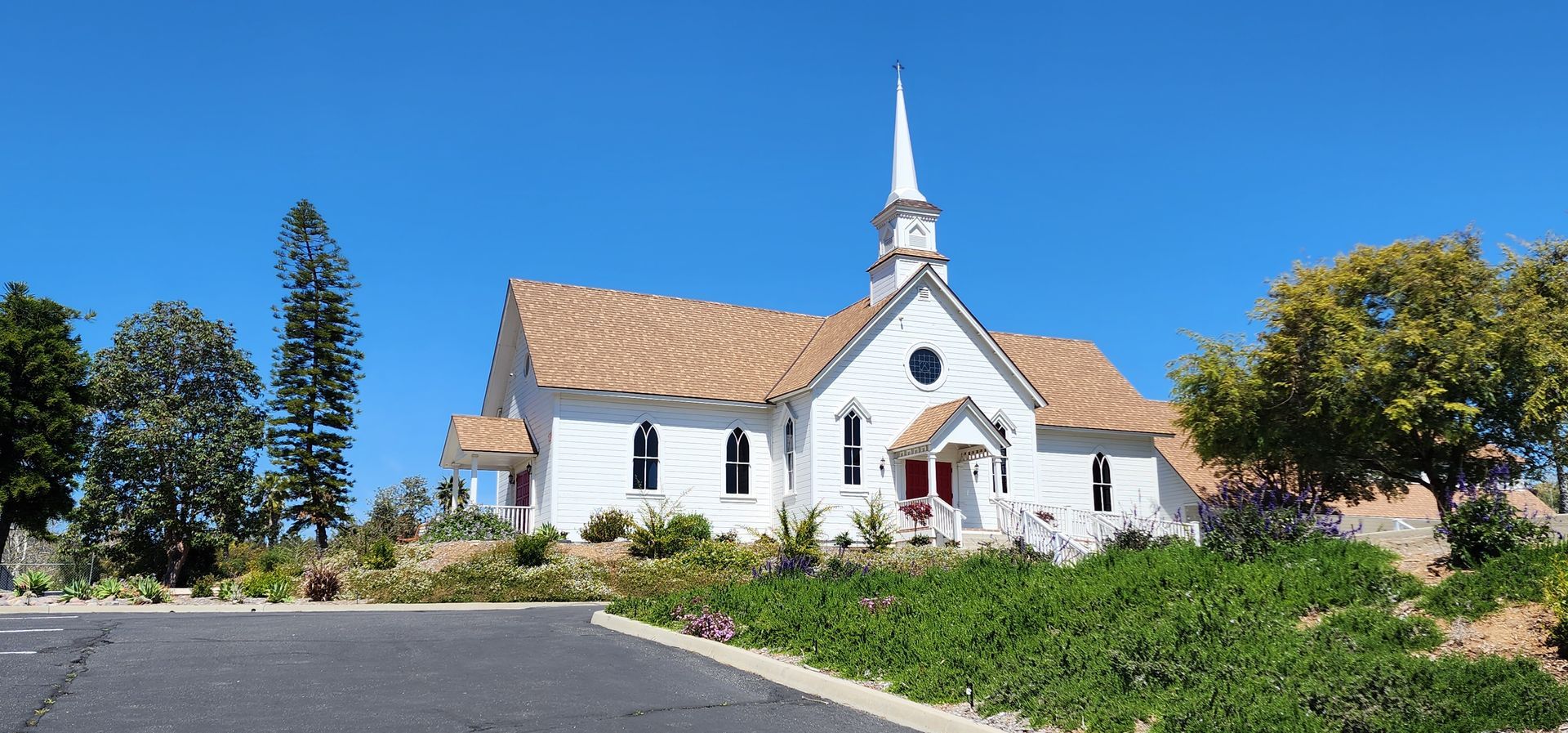 A small white church with a steeple is sitting on top of a hill.