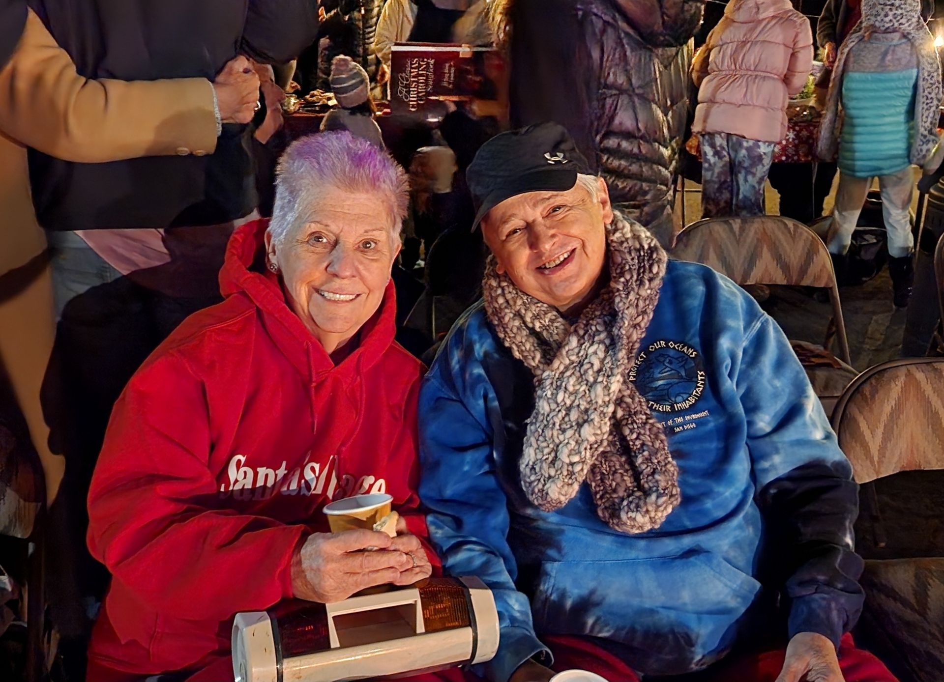 A man and a woman are sitting next to each other holding cups of beer.