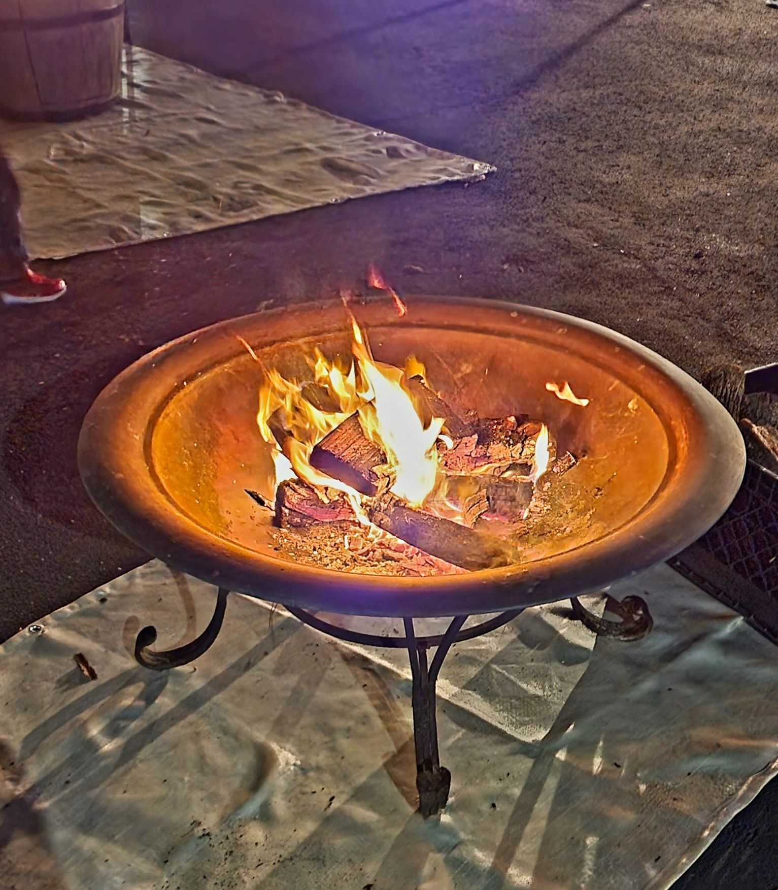 A fire pit is sitting on a blanket on the ground