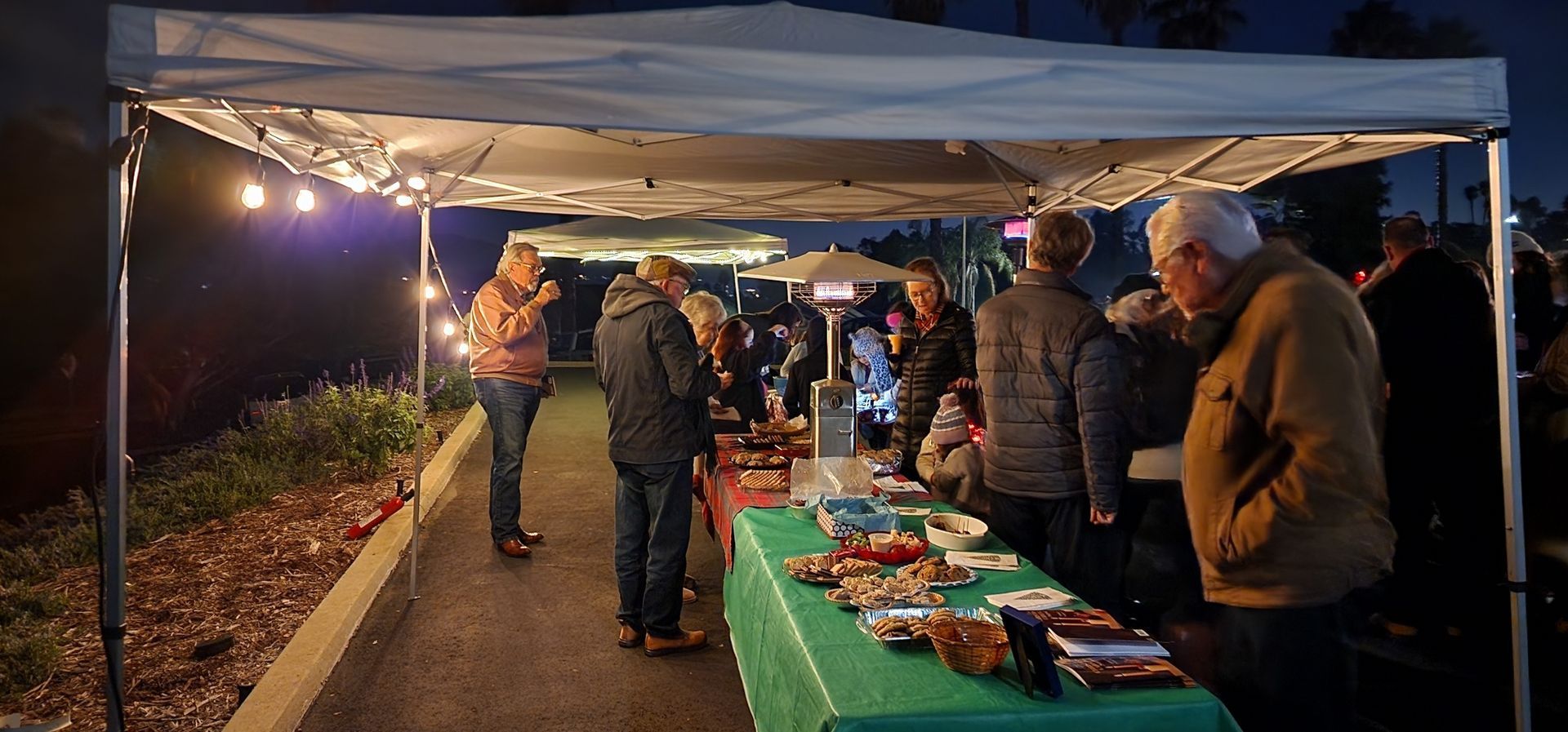 A group of people are standing around tables under a tent.
