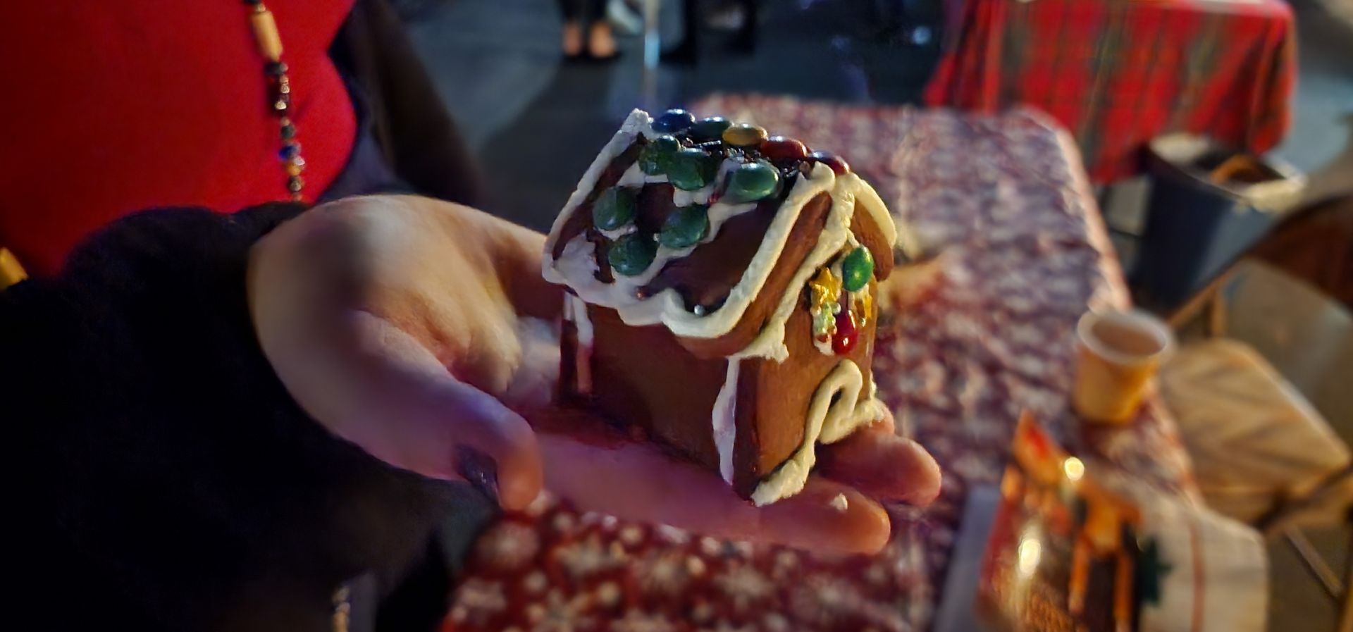 A person is holding a small gingerbread house in their hands.