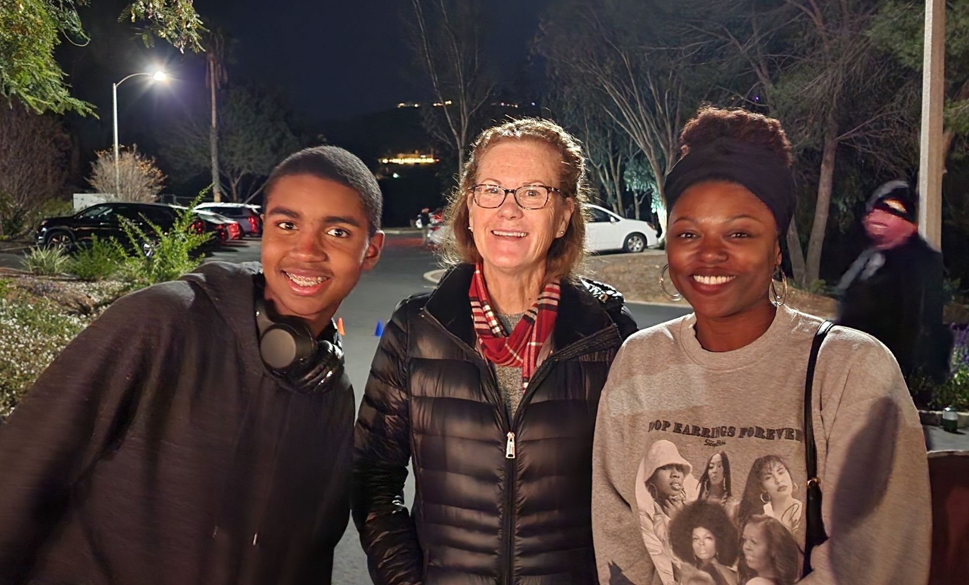 Three people are posing for a picture in a parking lot at night.