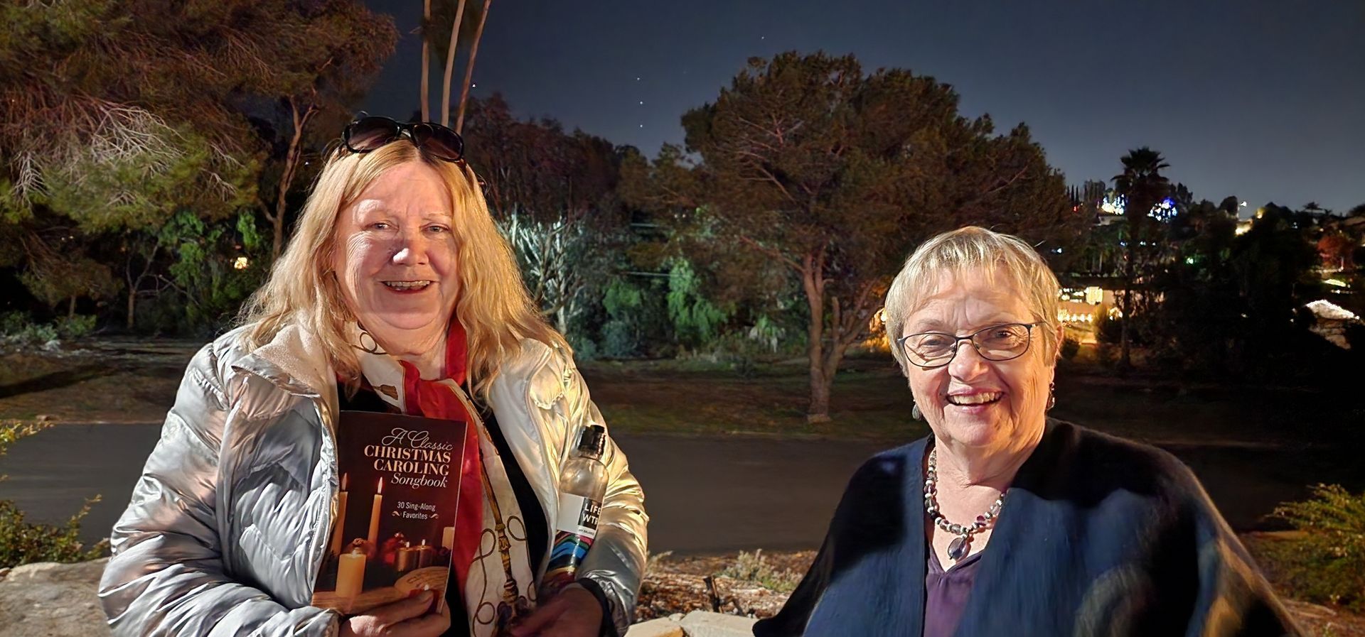 Two women are standing next to each other in a park at night.