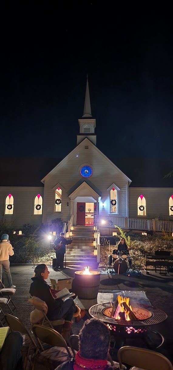 A group of people are sitting around a fire pit in front of a church at night.