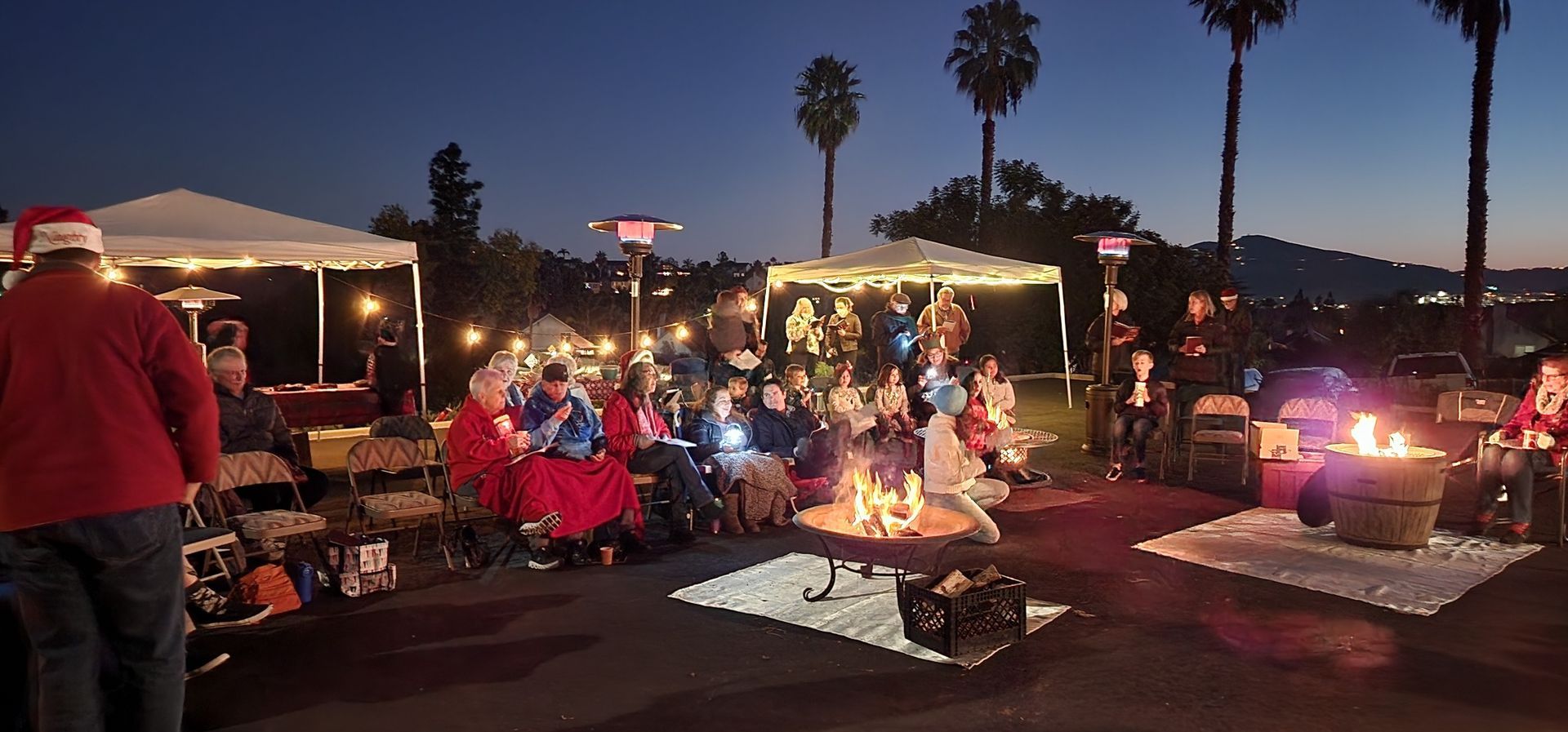 A group of people are sitting around a fire pit at night.