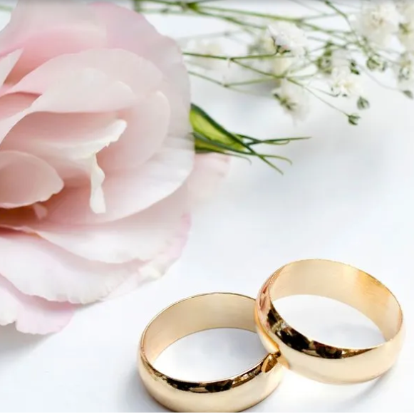 A pair of wedding rings next to a pink flower