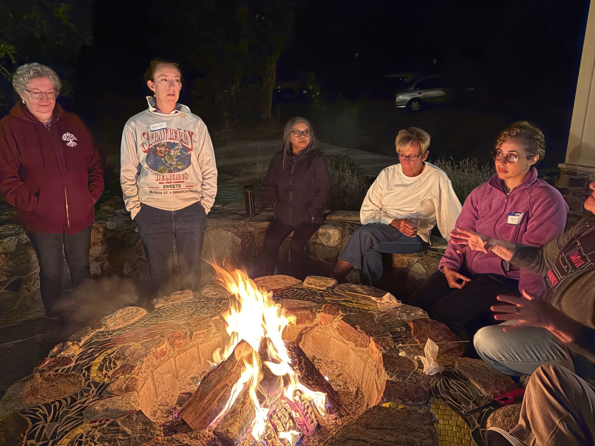 Group of people around a campfire at night, talking and enjoying the flames.