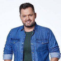 Een man met een baard draagt een spijkerhemd en een groen shirt.